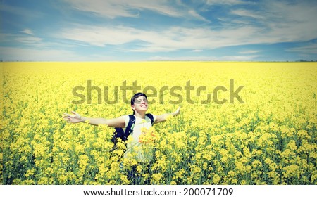 Young happy woman with backpack on a field of yellow rape