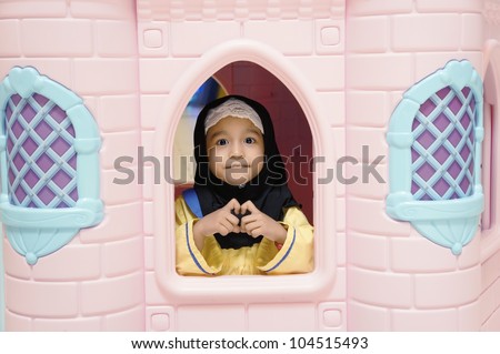 Cute Muslim girl playing at mini castle at preschool kindergarden.