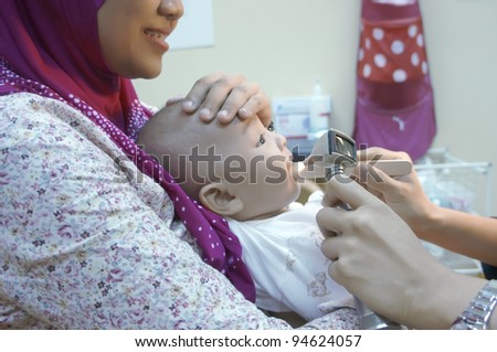 Doctor inspecting Muslim baby boy tongue for viral infection.