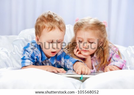 Little girl and boy read the book in the bed