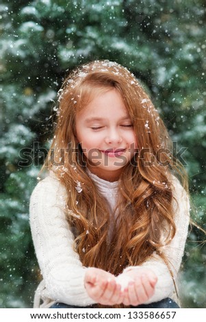 Beautiful little girl catches snowflakes