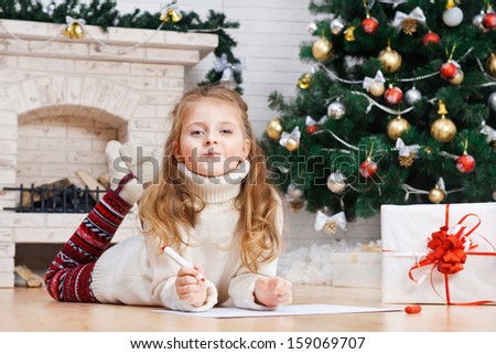Little girl writes letter to Santa near christmas tree