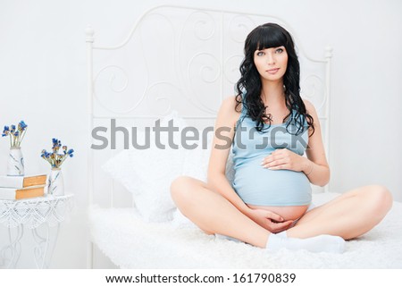 Pregnant woman sit on bed