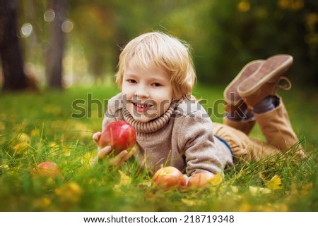 Happy child with red apples in autumn park