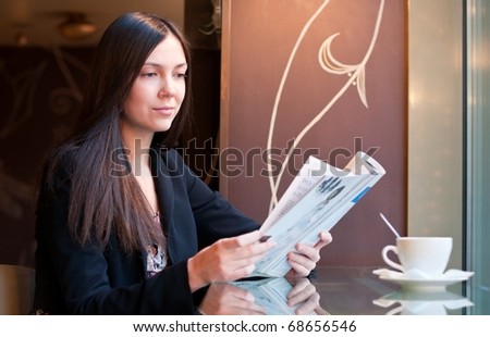 Attractive brunette young woman reads a magazine sitting in a cafe, shallow DOF, focus on face