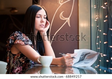 Attractive brunette young woman reads a newspaper sitting in a cafe, shallow DOF, focus on face