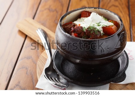 black pot on wooden table with hot meat and tomato