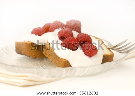 Photograph of pound cake dessert, with whipped cream  and raspberries, on glass plate