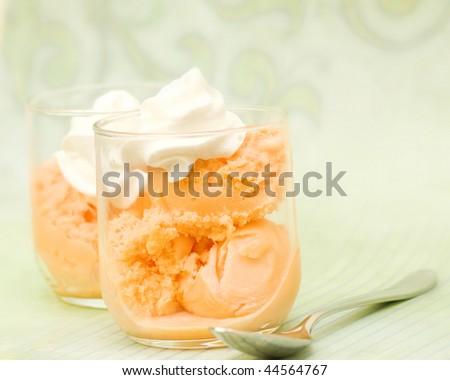 two orange gelato ice cream bowls, on green background with whipped cream