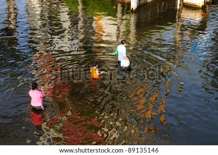 BANGKOK, THAILAND - NOVEMBER 19 -Thai family wade  through flood waters on the flooded street in Bangkok. A woman take photo her family  on Saturday on November 19, 2011 in Bangkok, Thailand