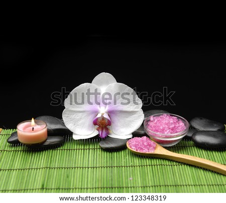 Pink orchid, candle with zen stone and sea salt in spoon on green mat