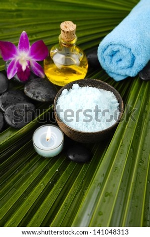 spa supplies with salt in bowl ,stones, candle, blue towel, massage oil, orchid