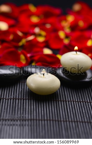 Many rose petals with white candle in stones on mat