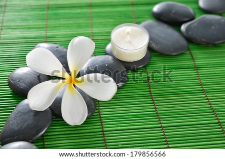 White frangipani flower and spa stones and white candle on green mat