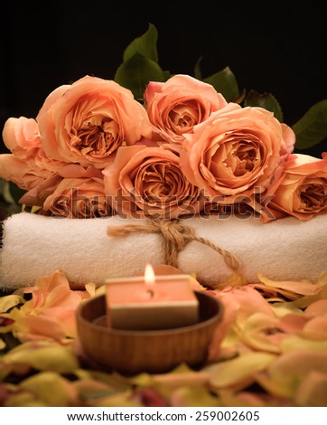 rose petals with candle in bowl with branch rose on towel on black