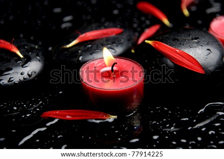 red candle with flower petals with black stones in water