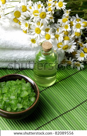 bouquet daisy on towel and Green bath salt in bowl with massage oil on green mat