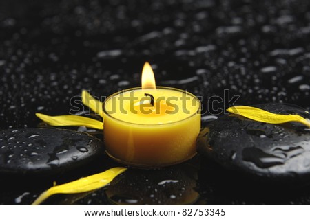Spa concept- candle with yellow flower petals in water drops as background.