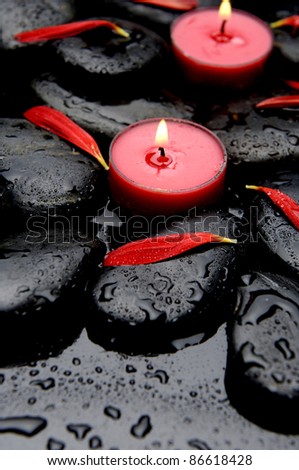 red candle with flower petals with stones in water drops