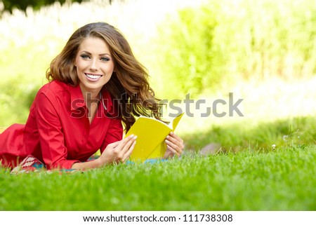 Young beautiful woman lays on green field and reads book.