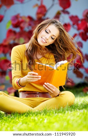 Young  woman lies on green grass and reads book against autumn  park.