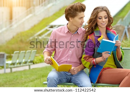 couple of students with  sitting at campus park and reading book.