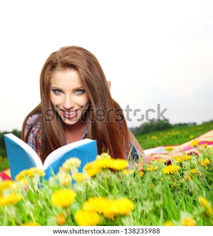 Beautiful girl lies on meadow and reads the boo