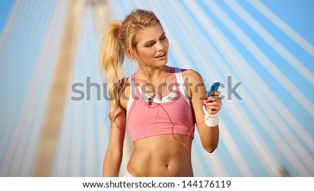 Stunning young blonde woman in pink sports bra rests and adjusting music on portable music player - smiling - fitness