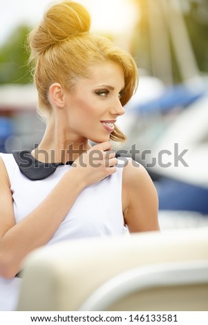 Beautiful sexy tanned brunette woman standing in a port fashion style, sea background, yachts
