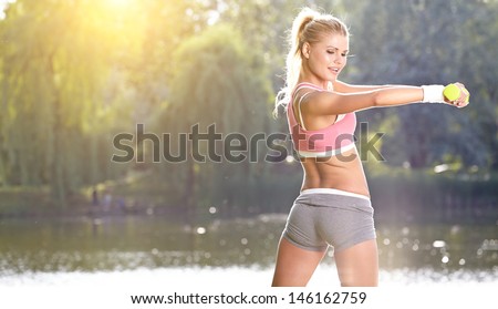 Female Fitness Instructor Exercising With Small Weights In Green Park