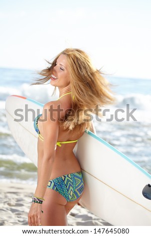 Rear view of beautiful young woman surfer girl in bikini with white surfboard at a beach