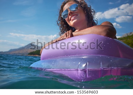 Portrait of lovely woman in bikini and sunglasses lying on mattress in sea
