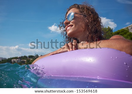 Portrait of lovely woman in bikini and sunglasses lying on mattress in sea