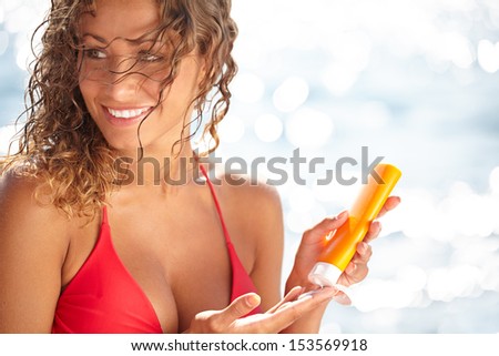 Young beautiful happy smiling cheerful tanned woman with sun-protection cream on beach, during sun bathing