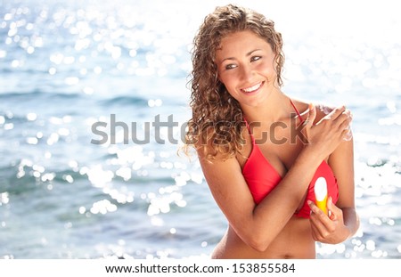 Young beautiful happy smiling cheerful tanned woman with sun-protection cream on beach, during sun bathing
