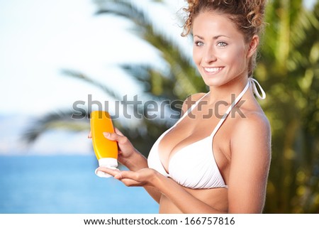 Sunscreen woman. Girl putting sun block on beach holding orange sun tan lotion bottle.