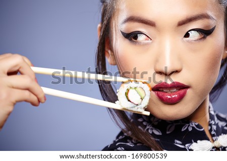 Sushi woman holding sushi with chopsticks looking at the camera smiling.