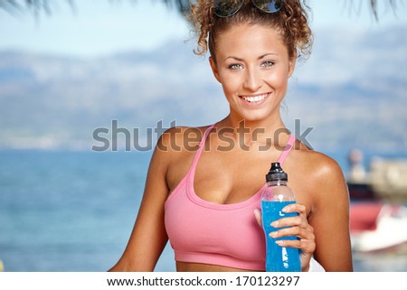 Fitness brunette drinking water and cooling off after running at the tropical beach