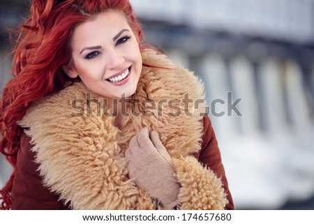 fashion portrait of a beautiful smiling girl with red hair in the winter