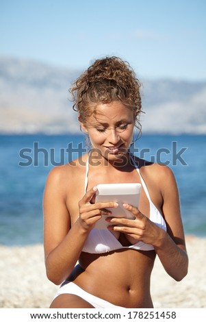 Woman with an e-reader on vacation at the beach reading a book.