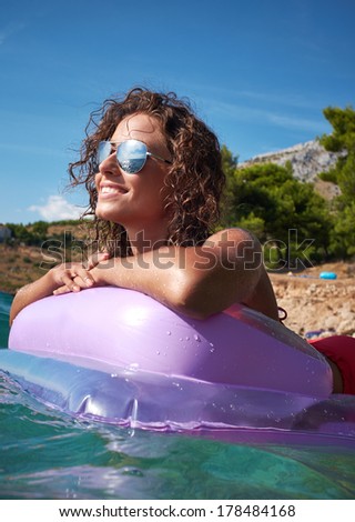 Young smiling woman having fun on pink air bed in sea water.
