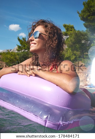 Young smiling woman having fun on pink air bed in sea water.