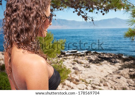 Sexy woman in white bikini near edge of infinity pool looking far on horizon.