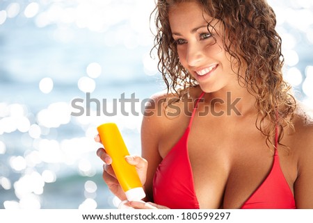 beautiful young woman in bikini smear protective cream on the skin on the beach under the sun