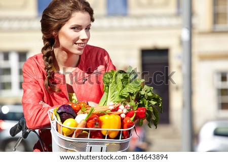 Pretty young woman with bicycle and groceries in old town street.