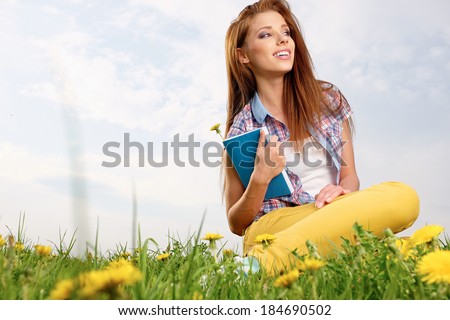 Young beautiful woman on green field and reads book.