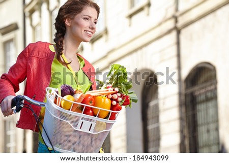 Pretty young woman with bicycle and groceries in old town street.