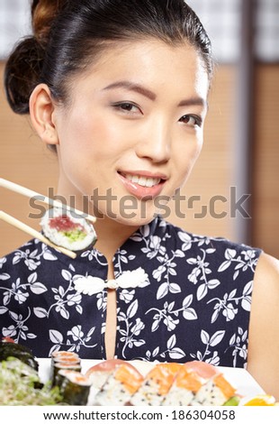 beautiful asian woman eating sushi with chopsticks