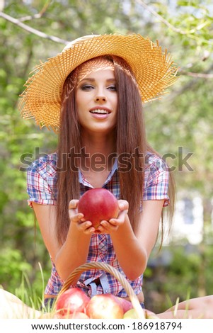 Smiling Young Woman Eating Organic Apple in the Orchard.Basket of Apples.