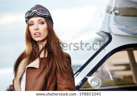 Portrait of young beautiful woman pilot in front of airplane.